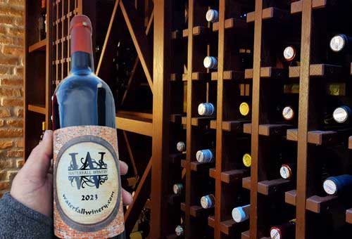 Waterfall Winery bottle in front of wooden wine racks.